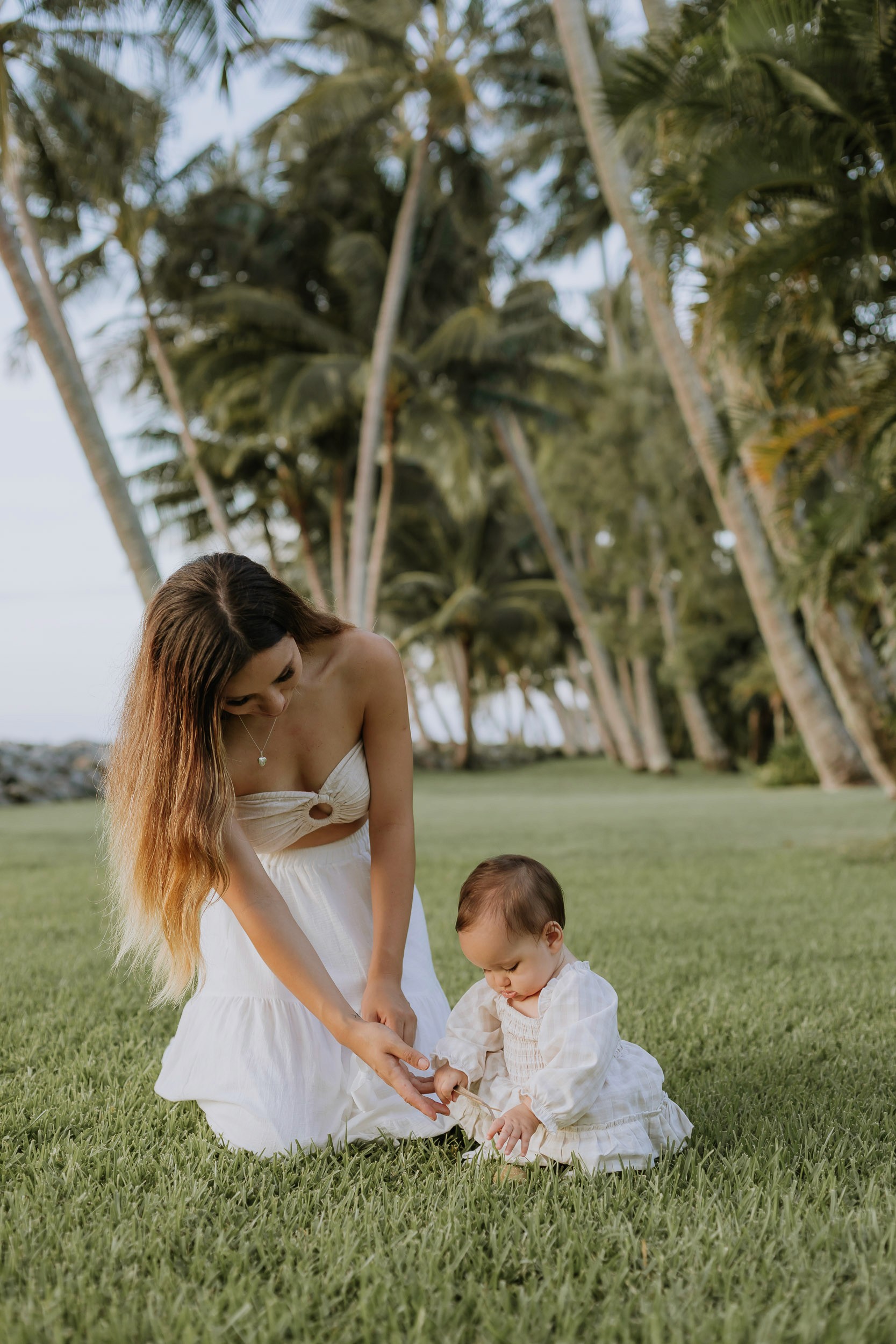Mum and daughter sitting amongst palm-lined path during a warm sunset family photography session