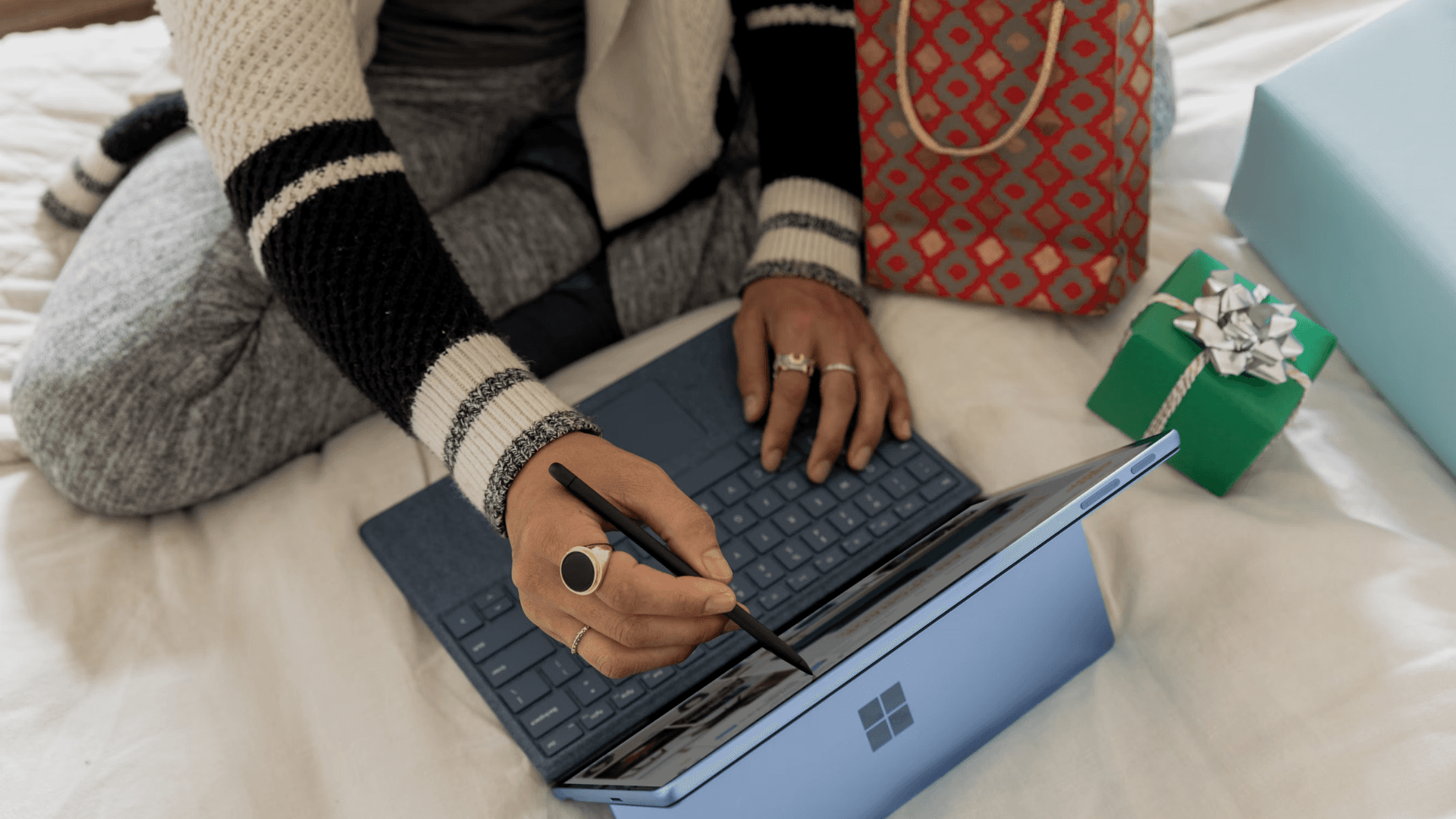 A close up shot of a person, sitting on a bed, using a laptop and surrounded by presents