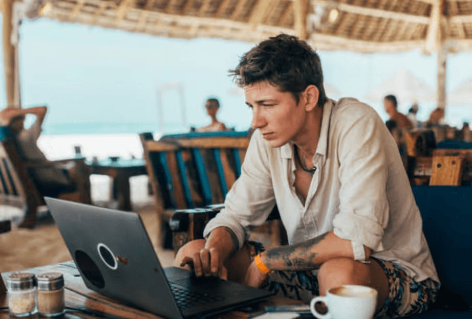 Man on laptop at beach cafe with coffee