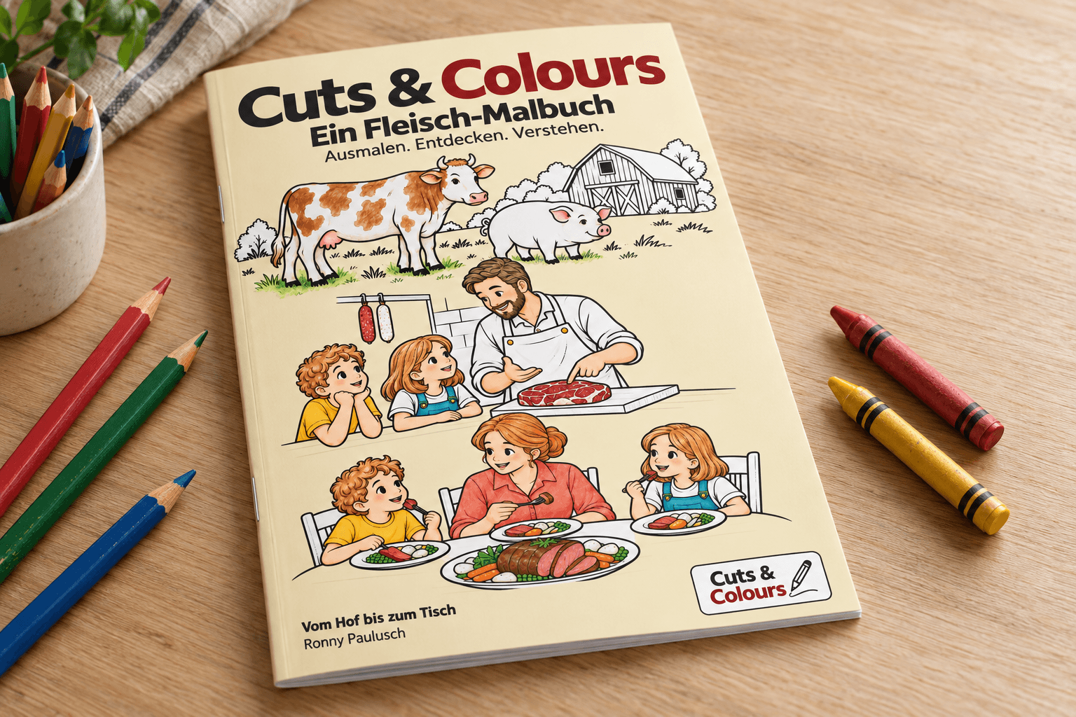 Das Malbuch Cuts & Colours liegt neben Bunt- und Wachsstiften auf einem Holztisch.
