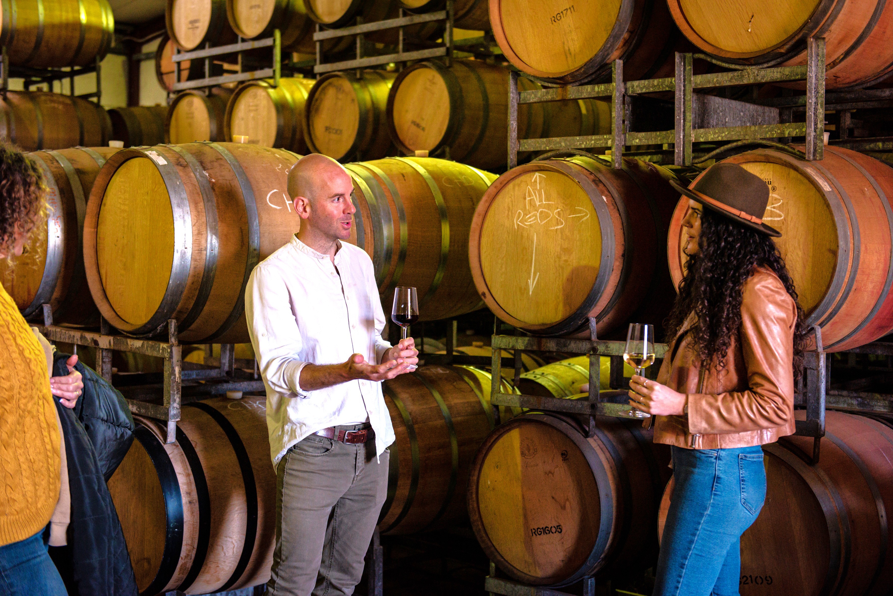 Tour guide explains wine making in the barrel room, with a glass in his hand. A lady carefully listens