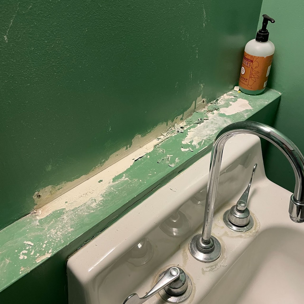 Bathroom wall and sink ledge with peeling paint before refinishing