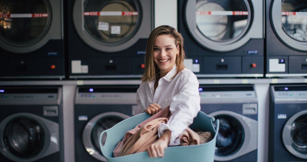 Smiling woman with laundry basket at a laundromat