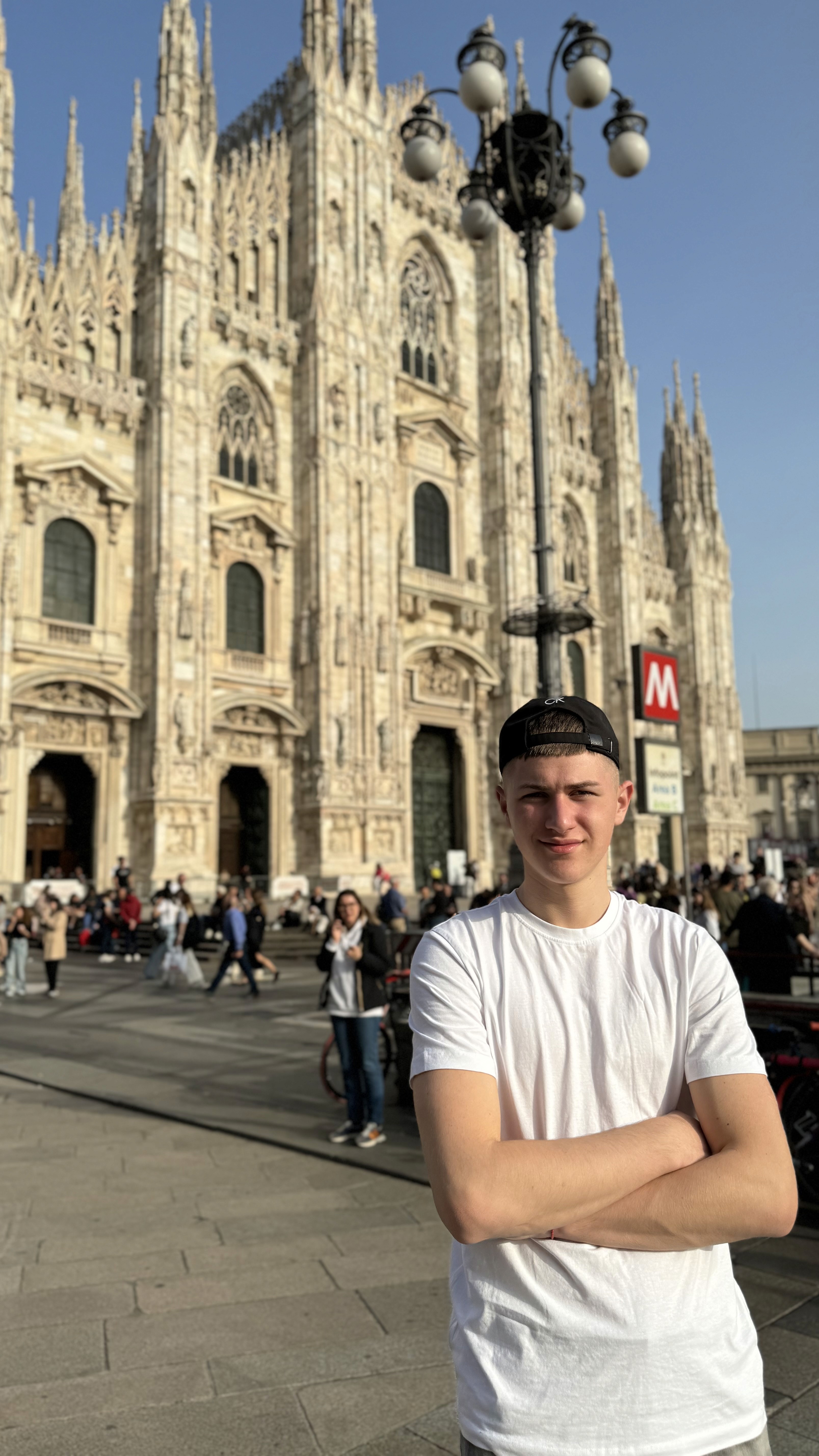 Portrait of a young woman with dark hair and green eyes, wearing a black top and gold necklace, set against a neutral background.