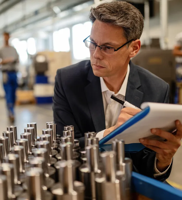 Quality inspector writing notes on a clipboard beside rows of machined metal cylinders