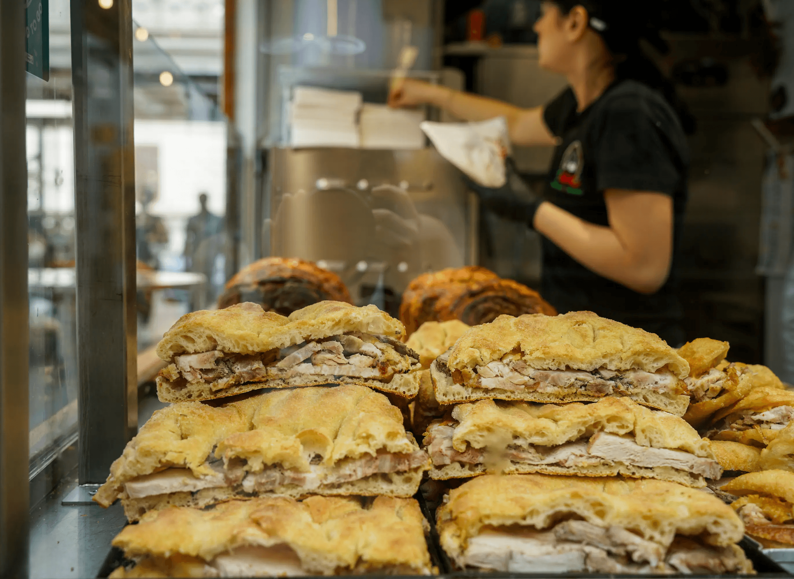 Sandwichs garnis exposés sur un comptoir du Mercato Testaccio à Rome, avec une vendeuse préparant des commandes en arrière-plan