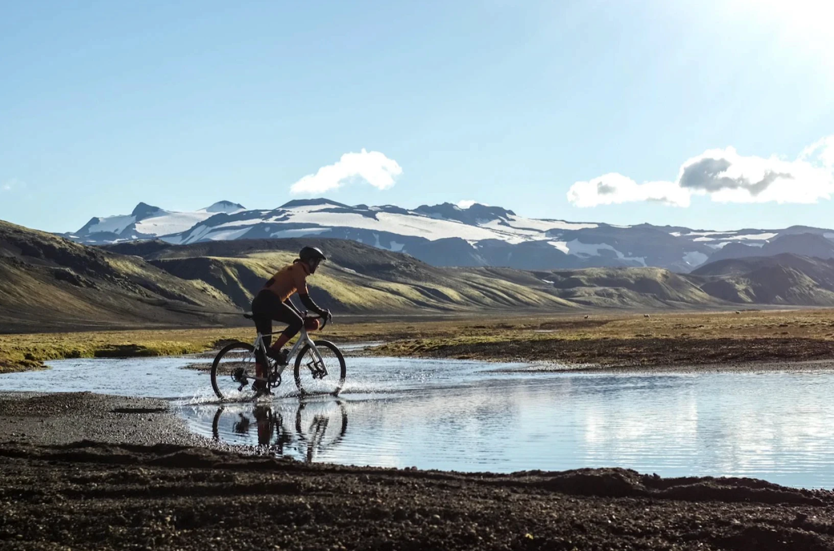 one cyclist crossing calm river in iceland with glacier in backround