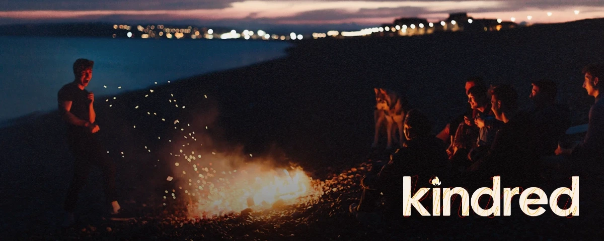 Title card graphic for Kindred. The Kindred logo sits atop an image of friends gathered around a beach campfire at sunset.