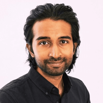 Person with dark, medium-length hair wearing a black collared shirt, face blurred, against a plain light background.