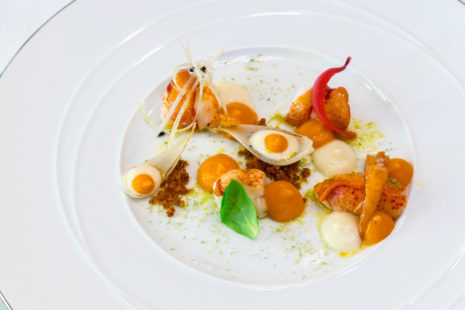 A gourmet seafood appetizer featuring cooked shrimp, hard-boiled egg halves, and orange spheres on a white plate with herbs.