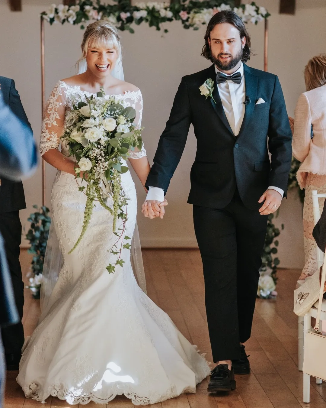 A smiling bride in a flowing ruffled gown holds a bouquet.