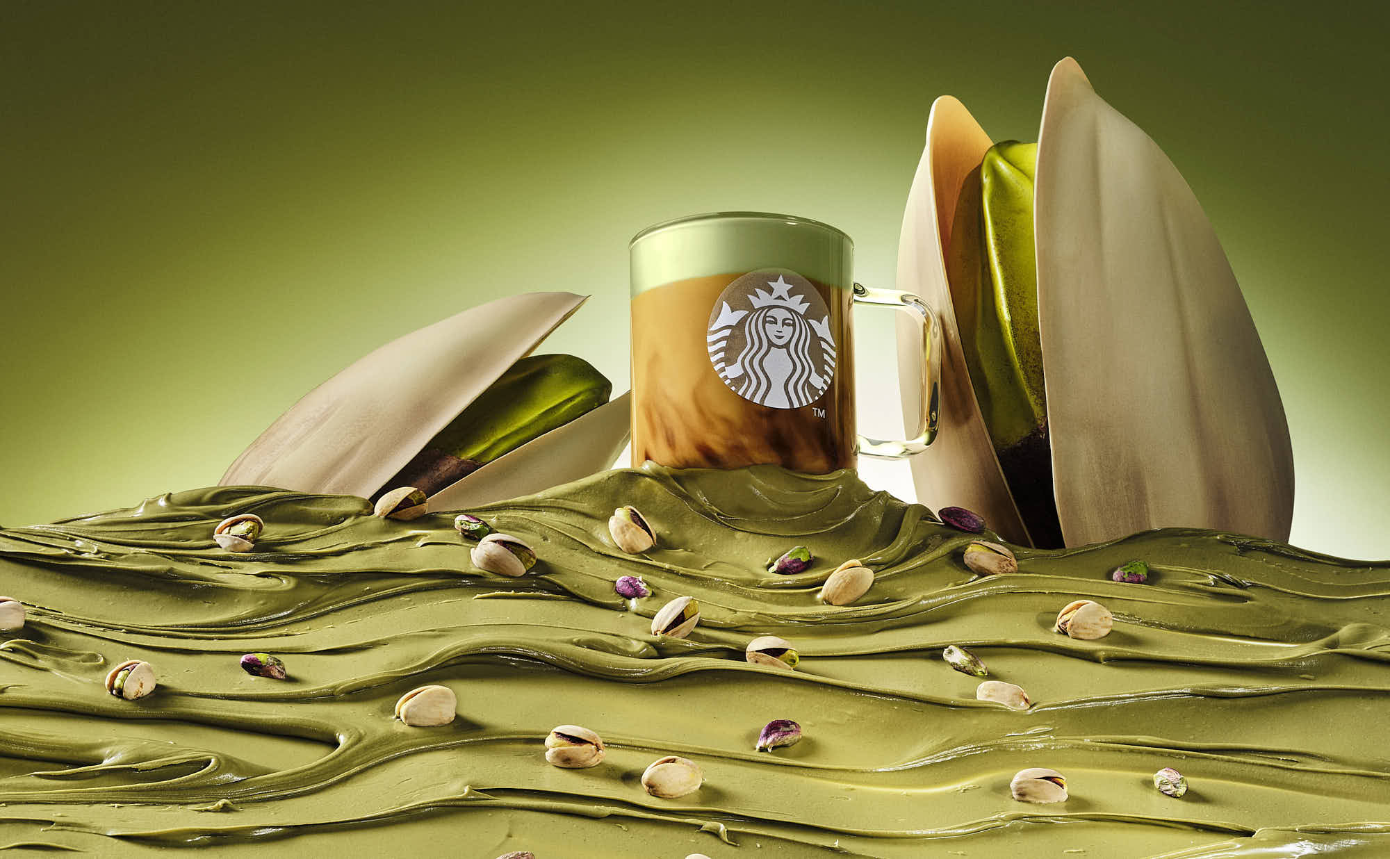 A heroic image of a coffee latte partially buried in golden green pistachio cream, with a soft green background with giant pistachio in shells.