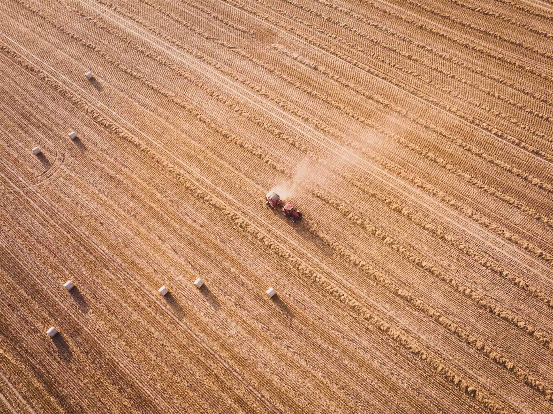 Aerial view of a tractor harvesting a wheat field, with rows of straw and hay bales representing the agricultural waste used in Strawtown's compressed straw building panels