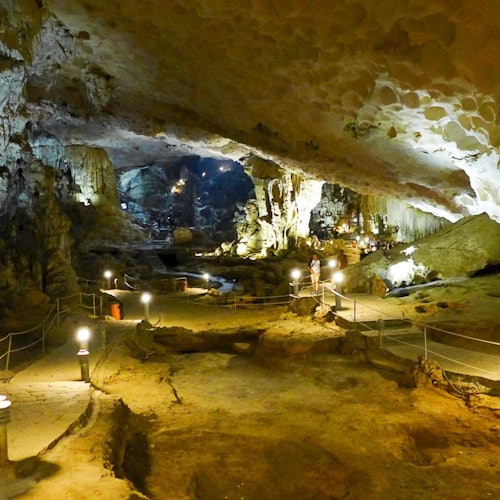 En rummelig, oplyst hule med stalaktitter, stalagmitter, en sti med gelændere og folk, der udforsker området.