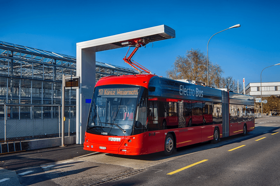 Autobus électrique rouge en charge à une borne de recharge publique, mettant en avant l'utilisation des transports publics électriques et le développement des infrastructures de recharge pour une mobilité durable en Suisse.