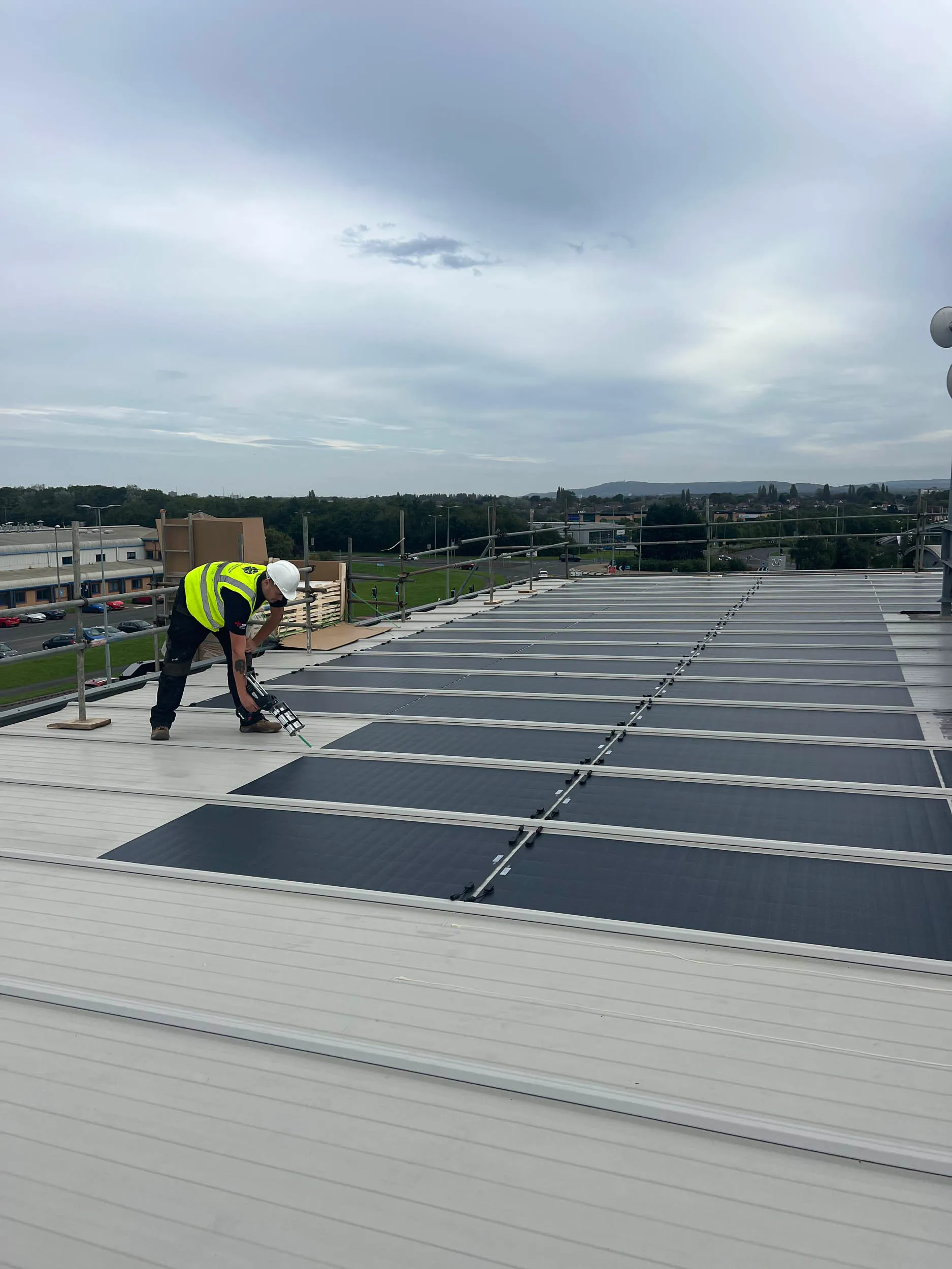 A large expanse of solar panels is installed on a sloped rooftop under an overcast sky, highlighting sustainable energy and renewable resources.