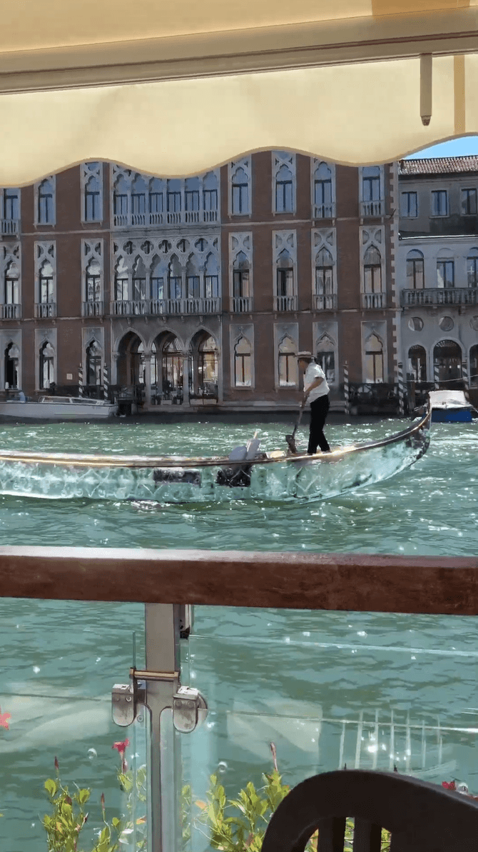 A gondolier navigates a transparent, ice-like boat through a Venetian canal