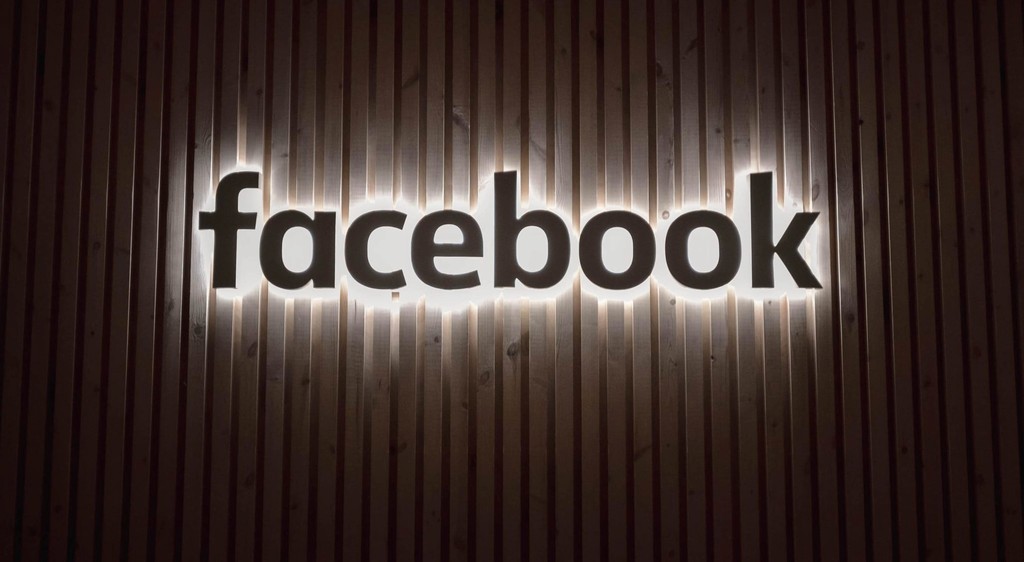 Illuminated Facebook logo on a wooden wall background.