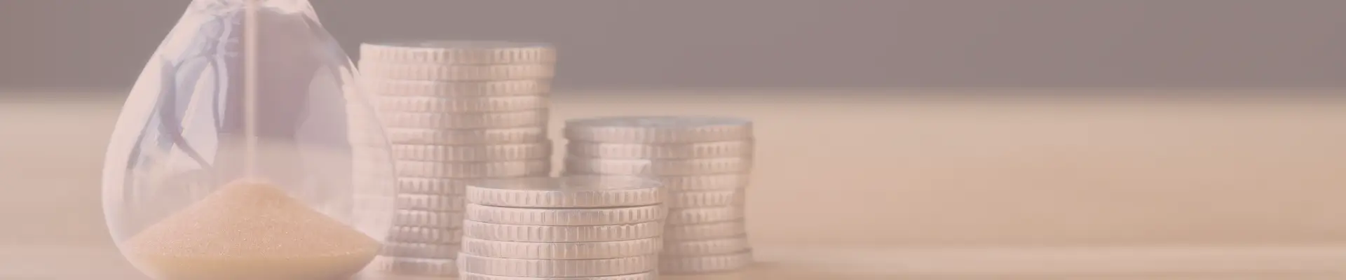 Hourglass beside stacked coins on a table—symbolizing the importance of timing purchases to maximize savings while shopping online.