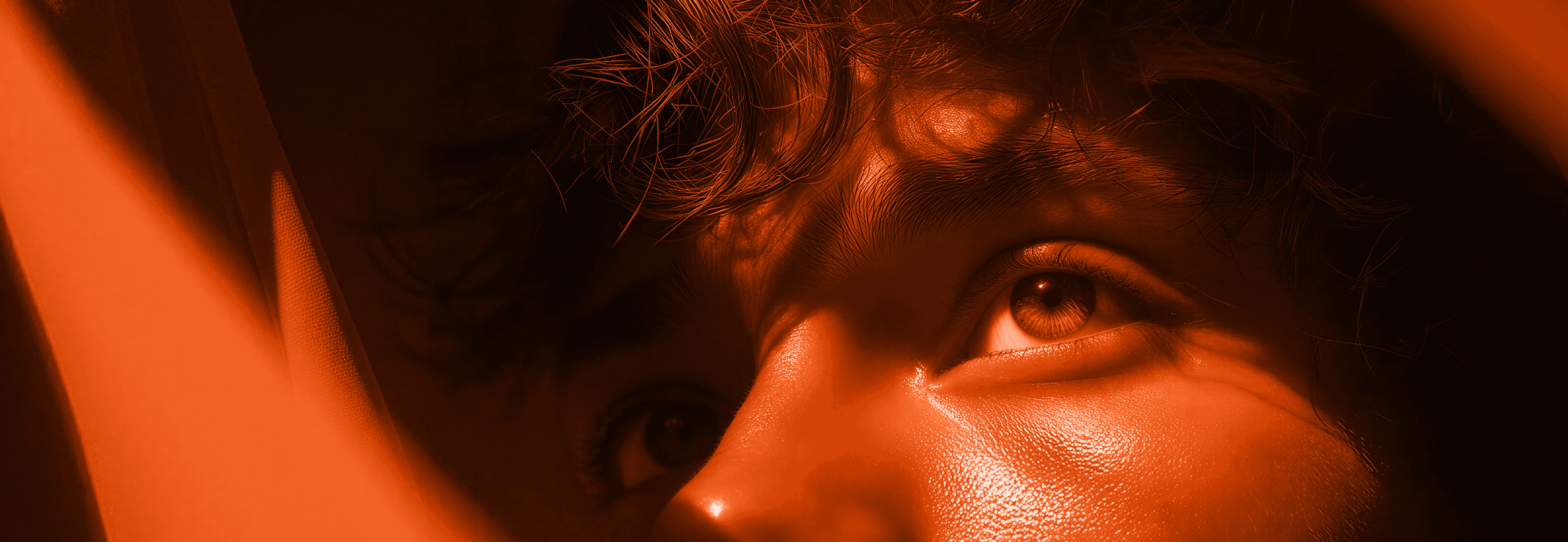 Close-up of a man's eye lit in warm orange light.