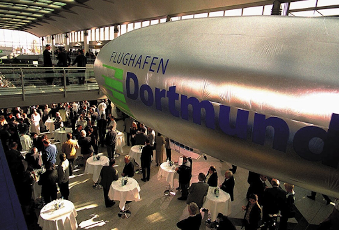 Menschen stehen bei Veranstaltung im Terminal unter Zeppelin mit Dortmund Schriftzug