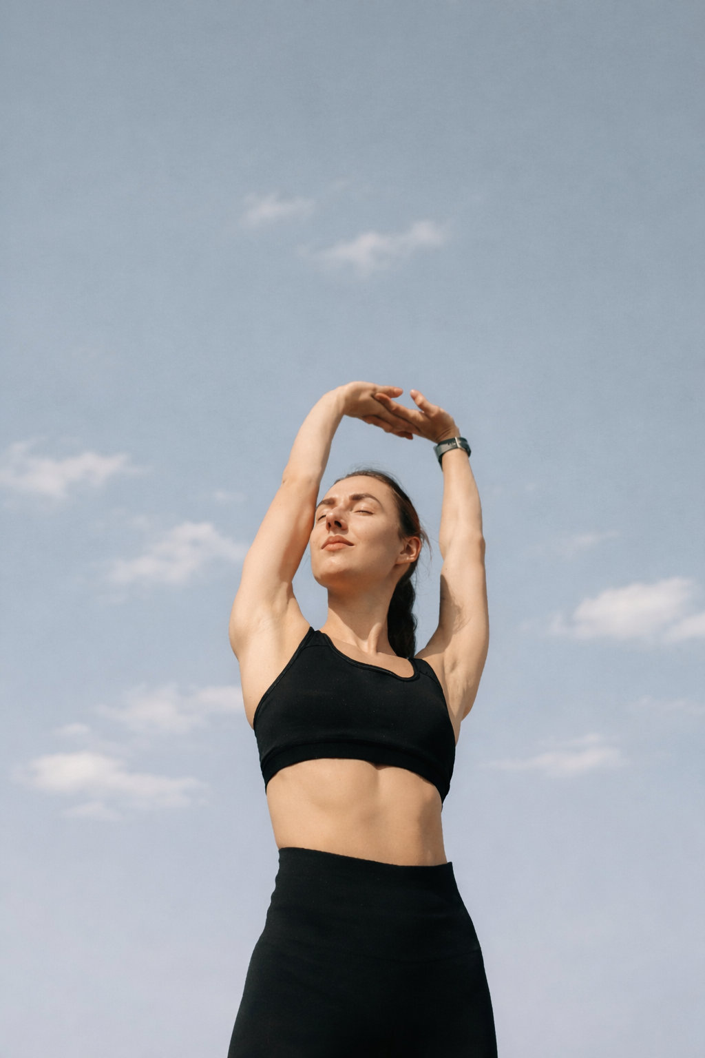 A woman in activewear reaching above her head to stretch