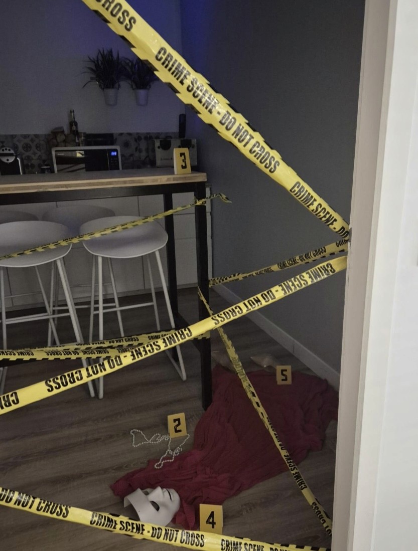 Simulation d'une scène de crime, avec des rubans "Crime Scene", indices numérotés, masque et drap rouge. 