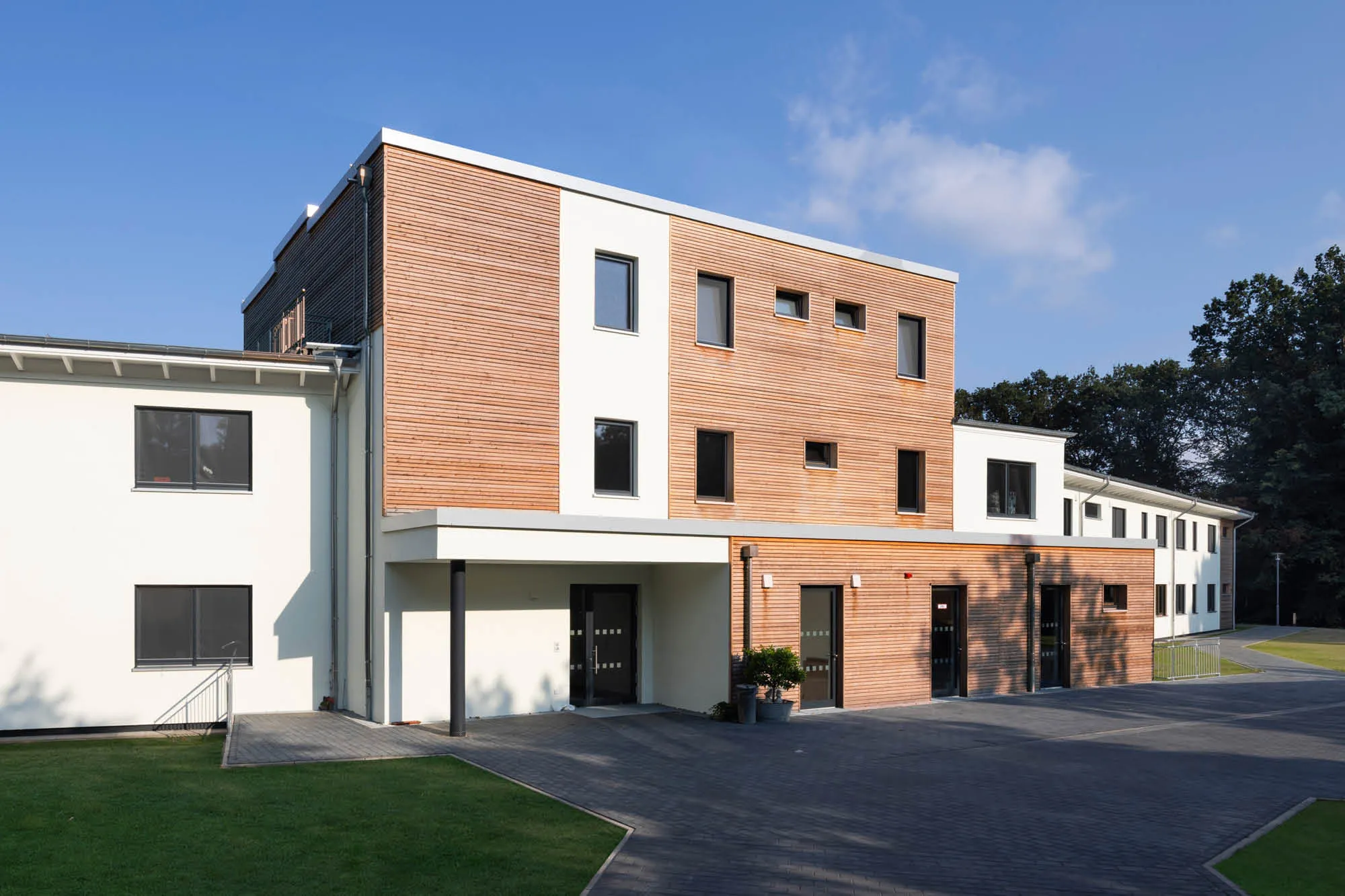 Modernes Holzfassaden-Gebäude mit zwei Stockwerken und weißem Putz, unter klarem blauen Himmel.