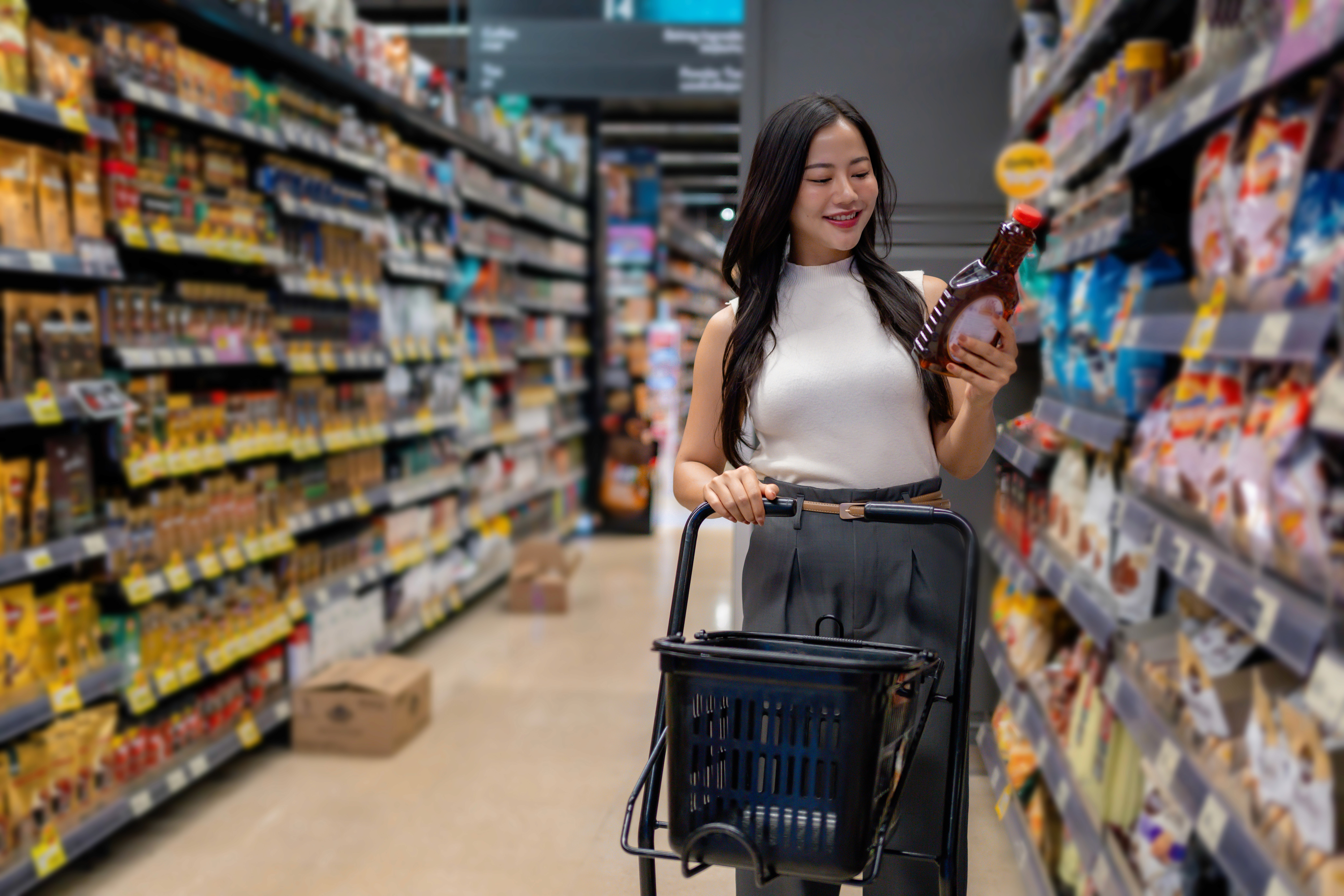 Girl customer reading ingredients of a product with shopping cart in one hand standing in a super market