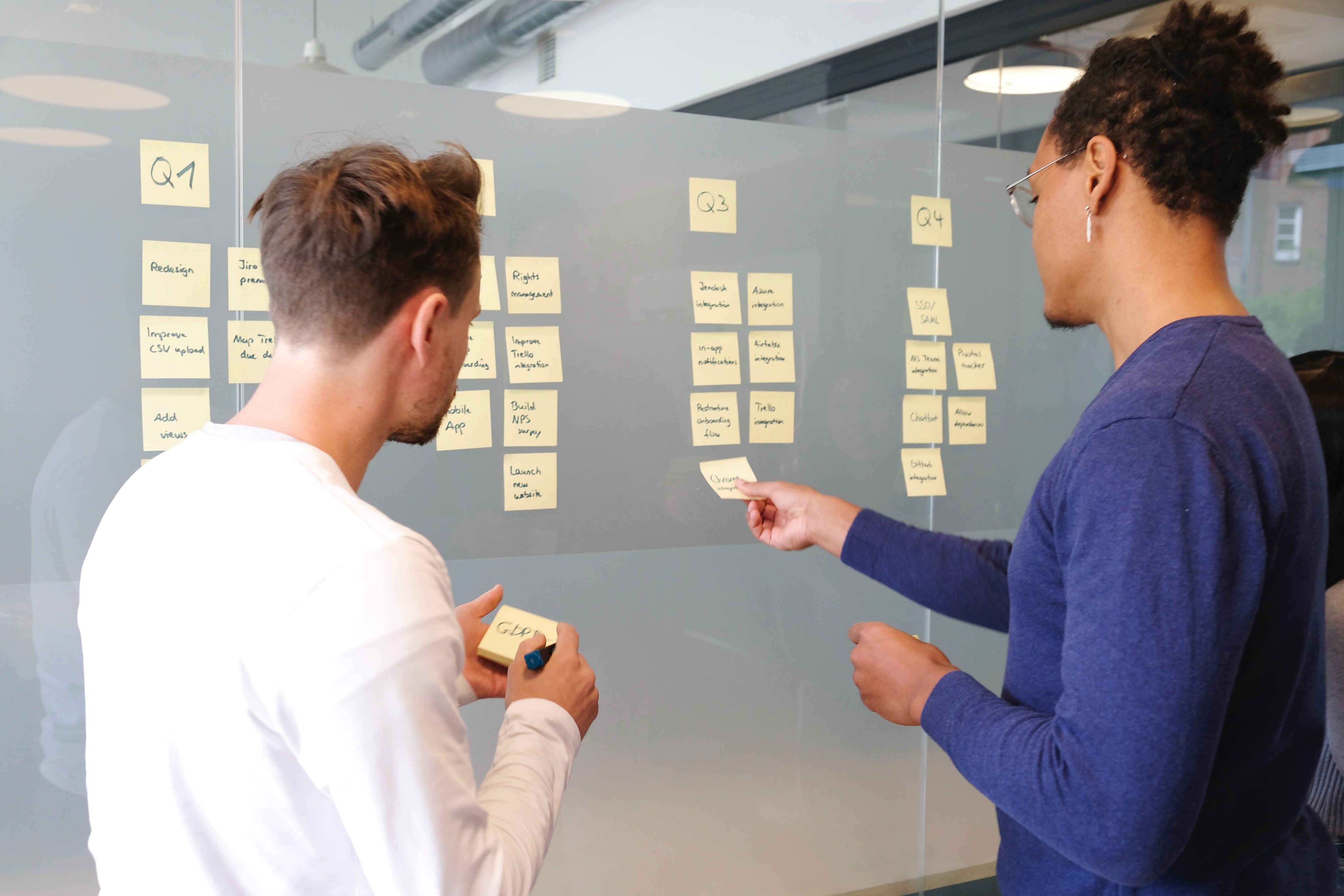 Two people facing a glass wall discussing and moving around yellow stickies