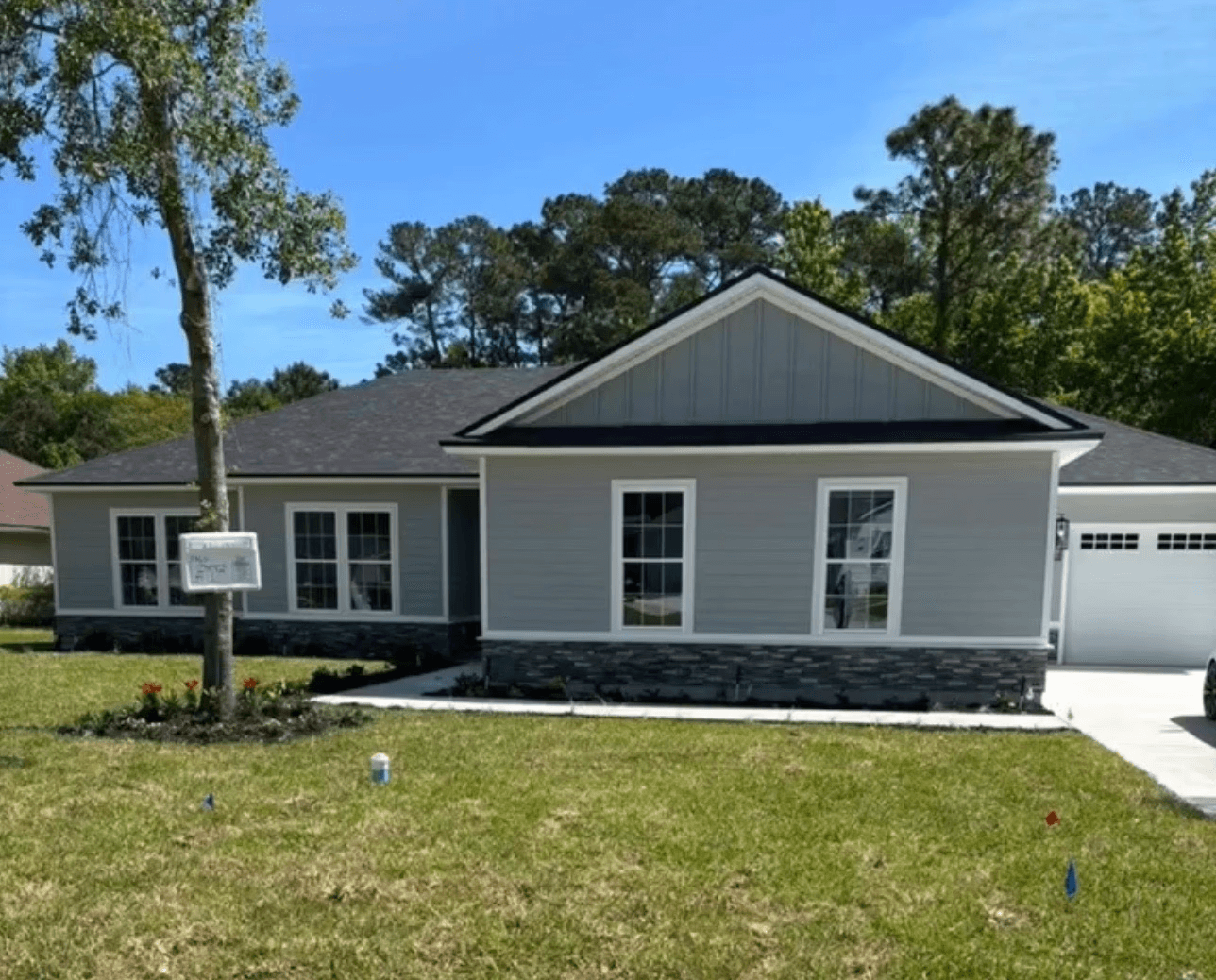 Gray house with stone accent base, lush green lawn, single garage, and blue sky