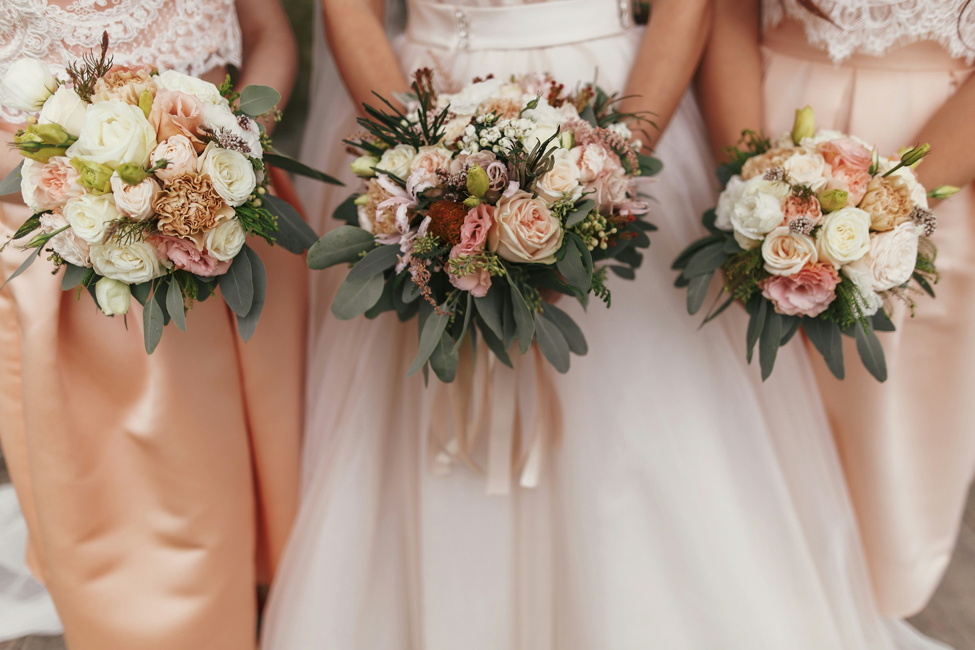 Bride and bridesmaids in peach blush dresses holding flower bouquets.
