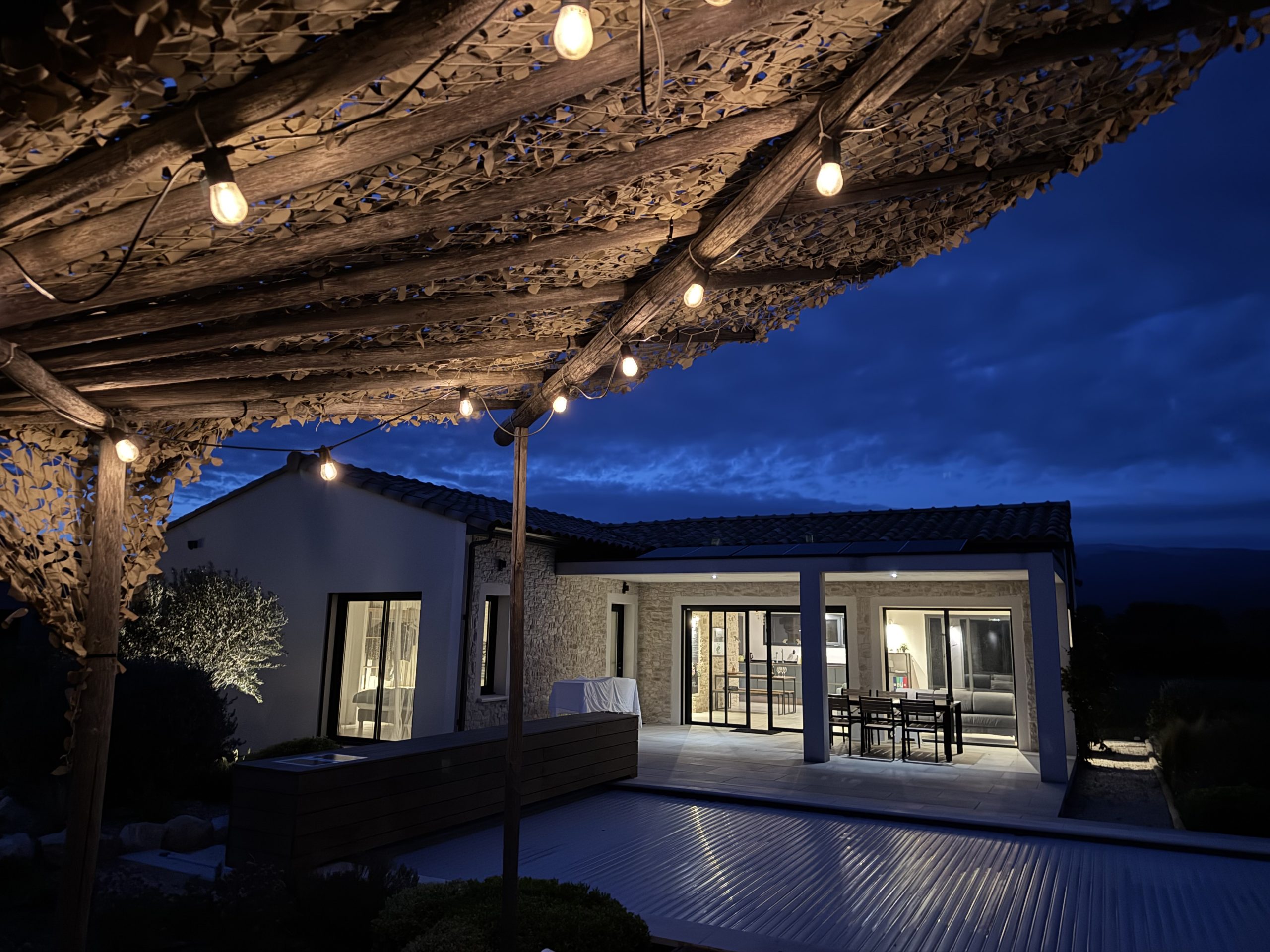 Maison de luxe éclairée la nuit avec terrasse et piscine. Ambiance chaleureuse et romantique.