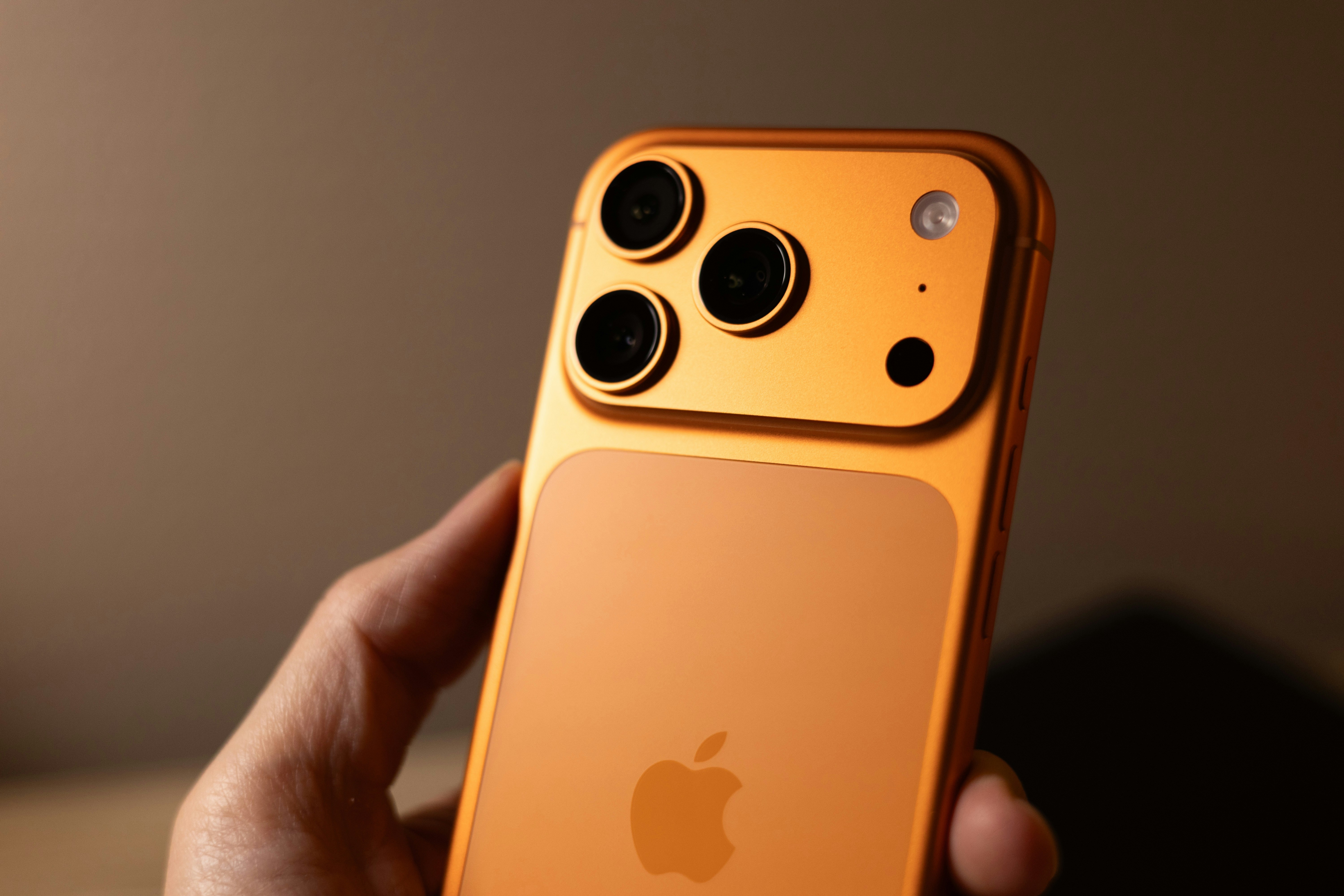 Orange smartphone with triple camera system held.