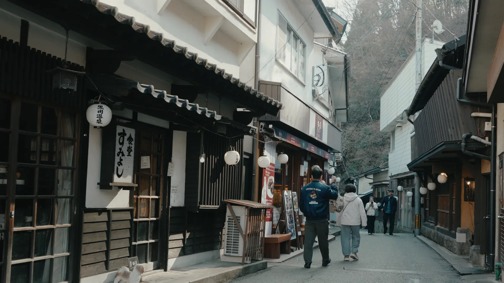 Shopfronts hung with noren along the main lane at Kurokawa Onsen, walkers passing