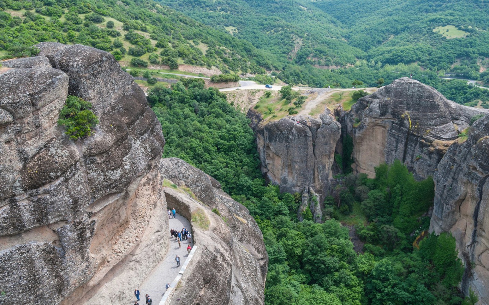 Wandelaars op een smal pad langs de rotsachtige kliffen van Meteora, Griekenland.