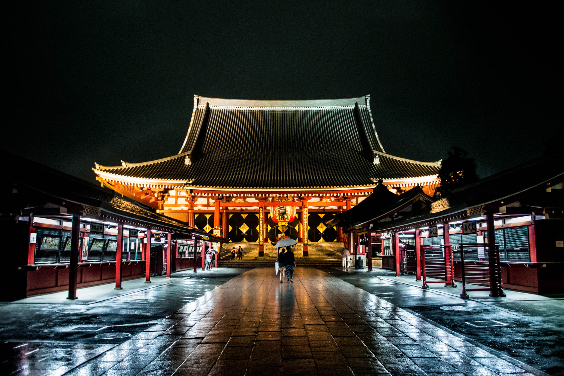A person walks toward a traditional Korean palace gate illuminated by warm lights at night under a dark sky.