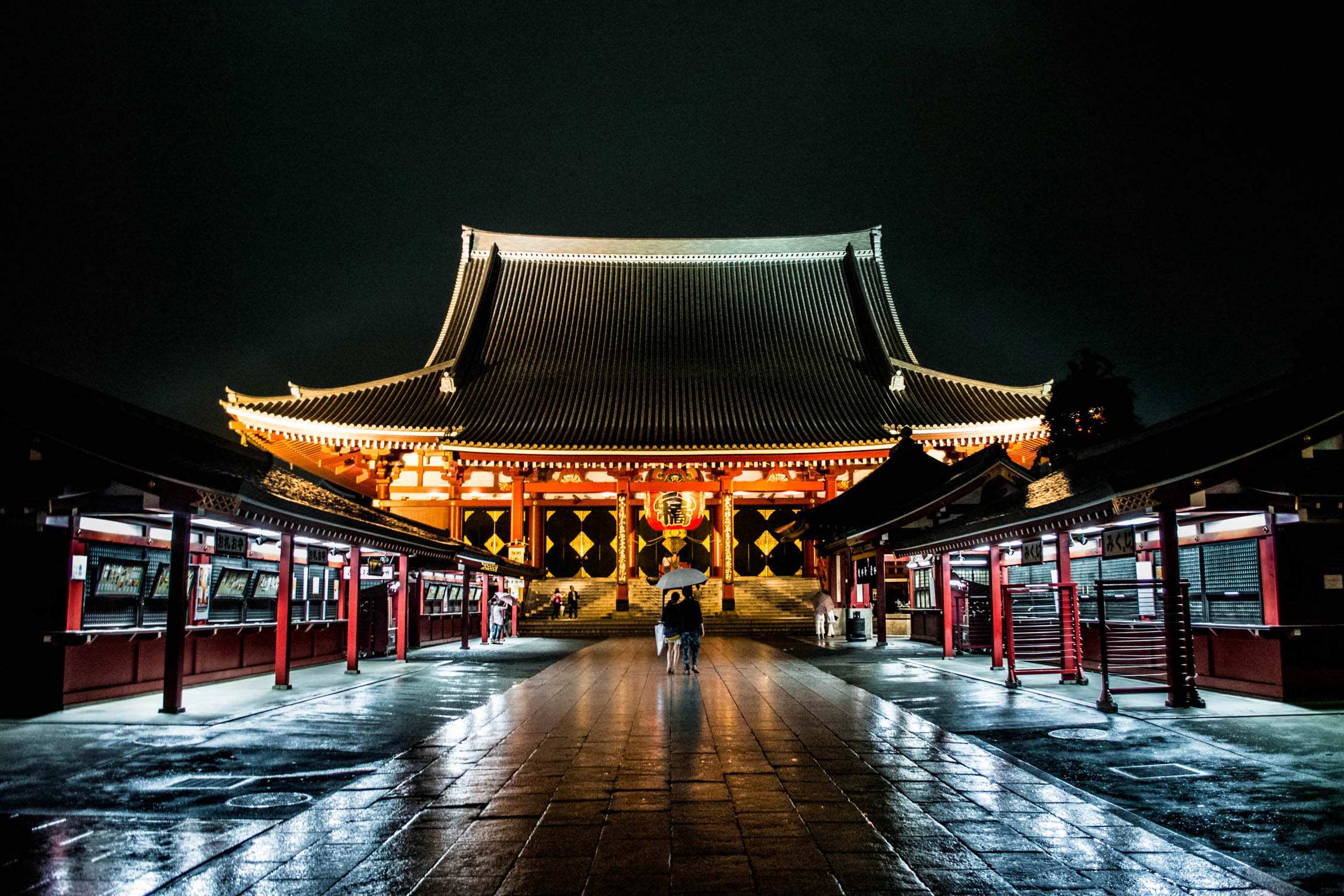 A person walks toward a traditional Korean palace gate illuminated by warm lights at night under a dark sky.