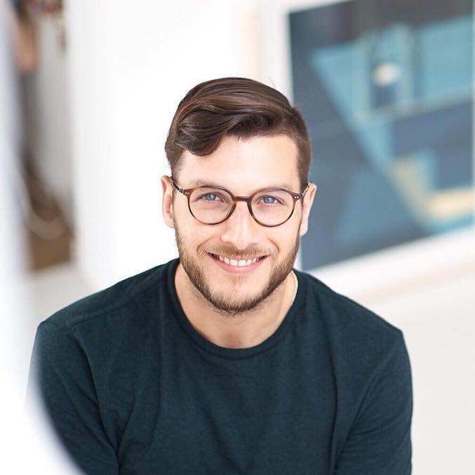 A woman with short curly hair wearing a black t-shirt looks into the camera.