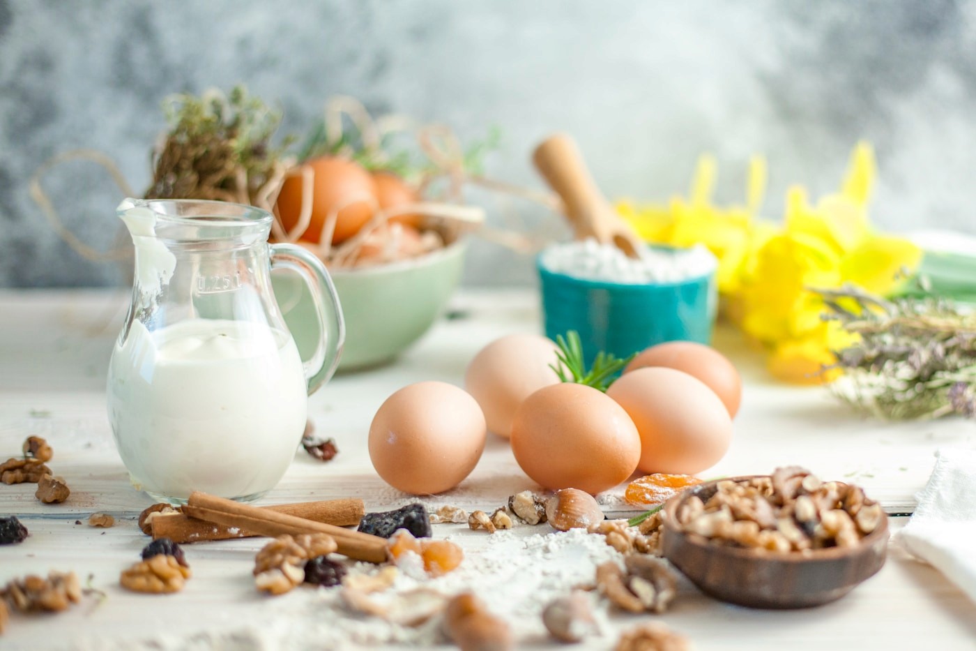 A table set with a jug of milk, brown eggs, and mixed tree nuts, several of the nine major food allergens
