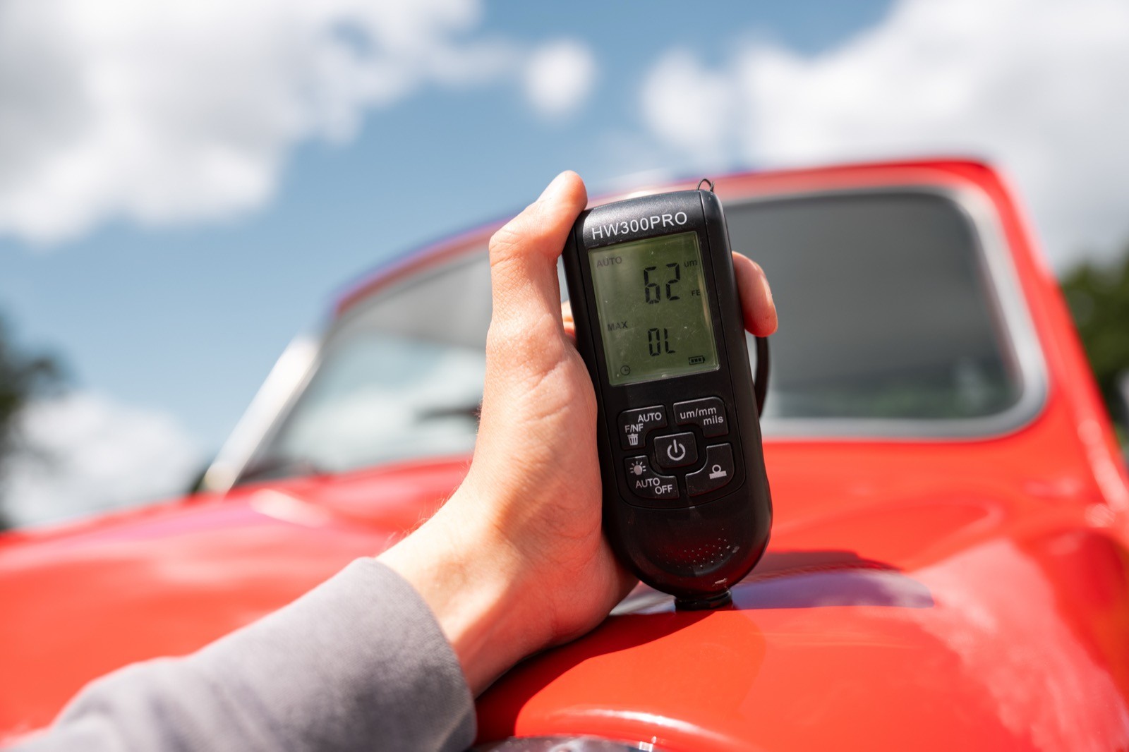 A hand holds a device displaying a screen, with a red car and blue sky in the background.