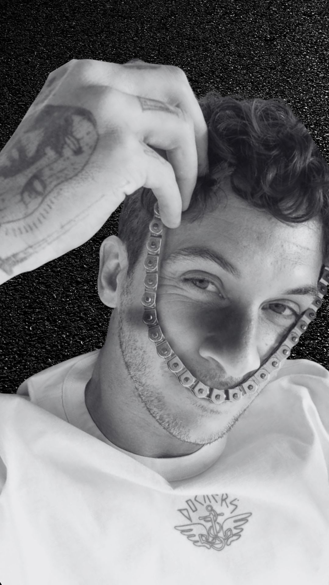 Image with a guy wearing a mask and has tattoos forming a heart with his fingers