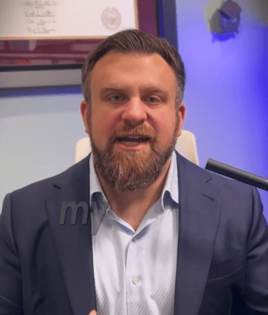 A person wearing the grey coat smiling in a cozy sunlight