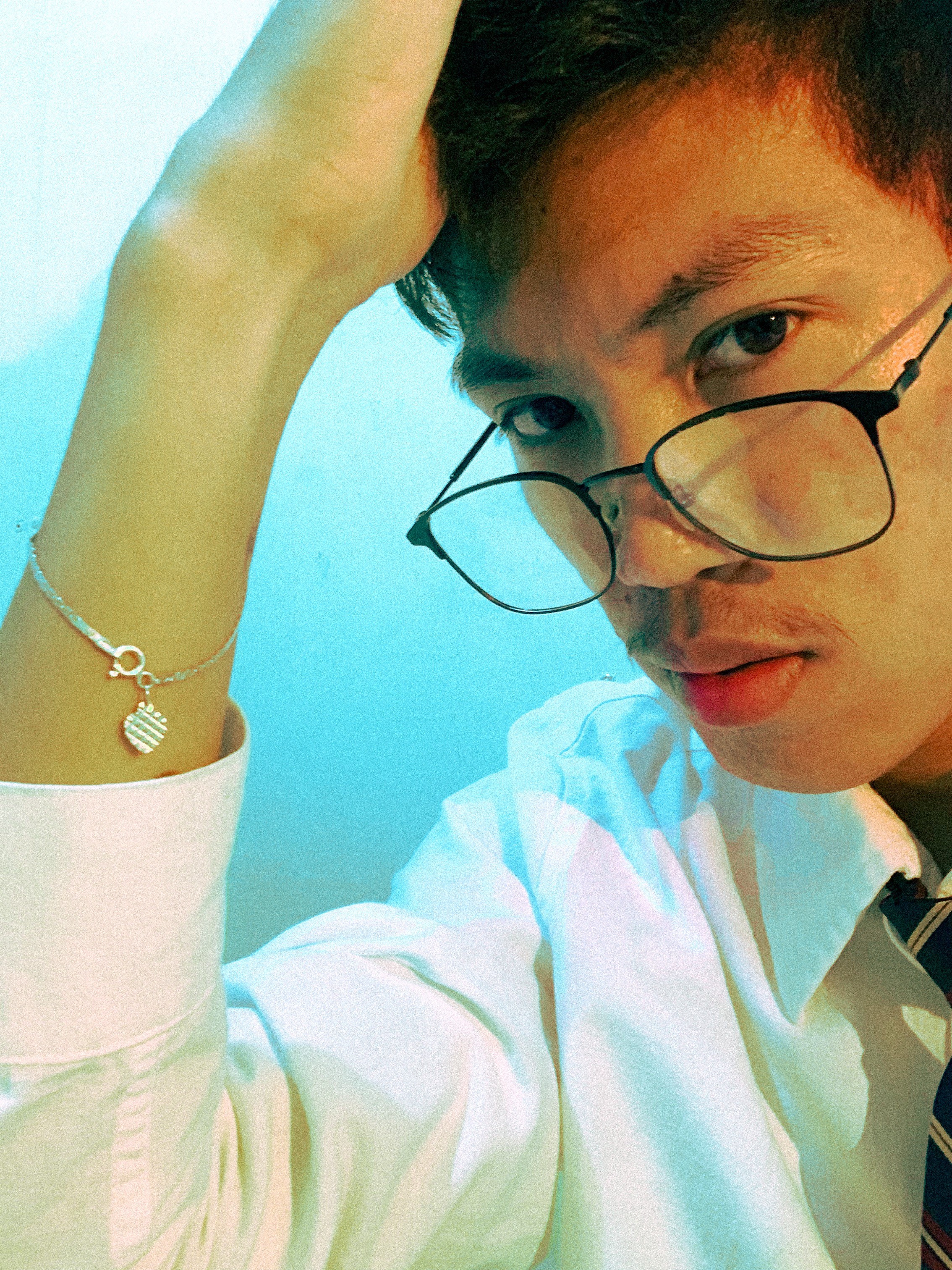 Man sitting in a dimly lit room, wearing a beige shirt and looking contemplative.