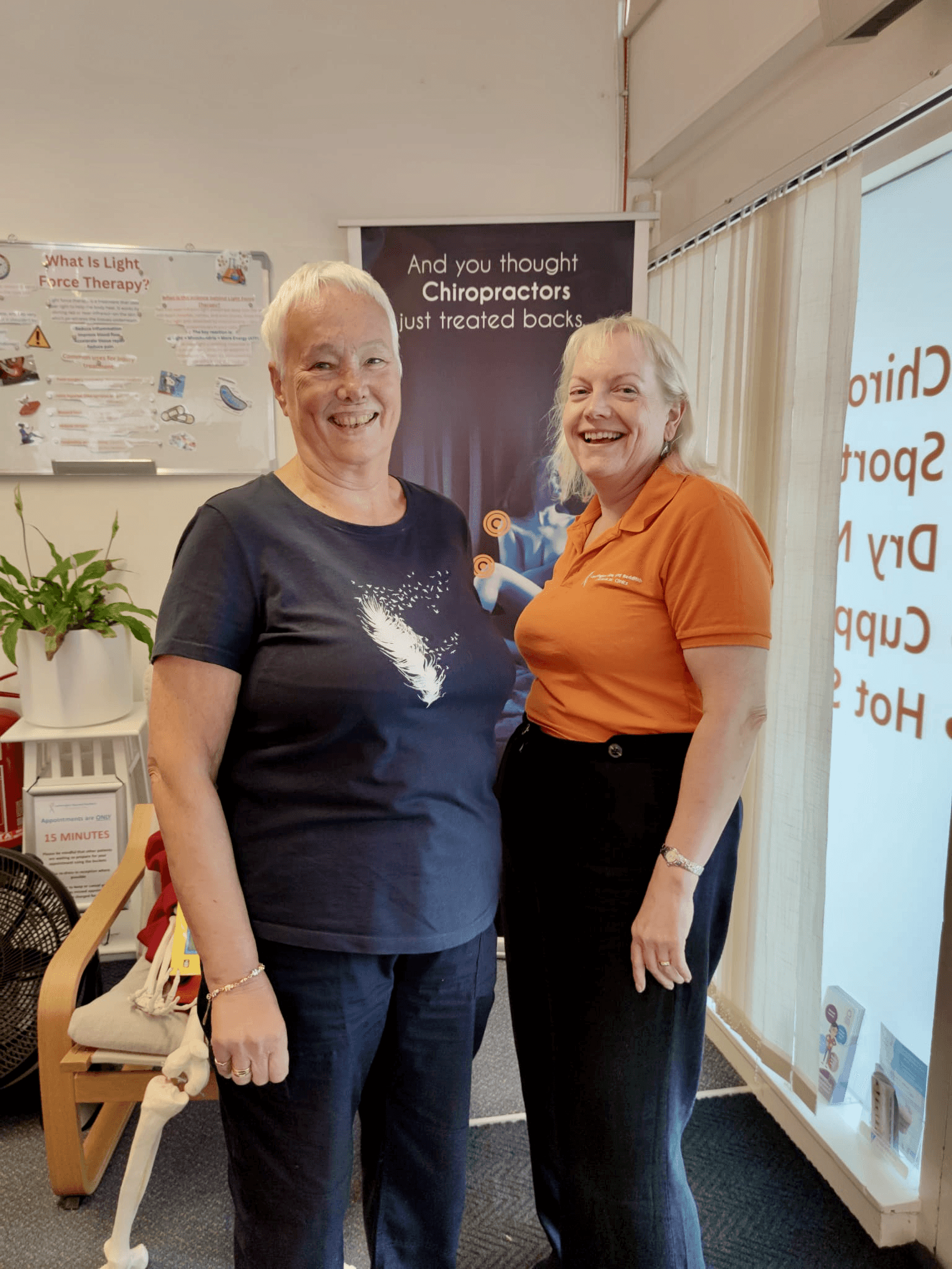Liz talking to a patient after her treatment in the chiropractor's clinic. One woman wears a navy shirt, the other an orange shirt.