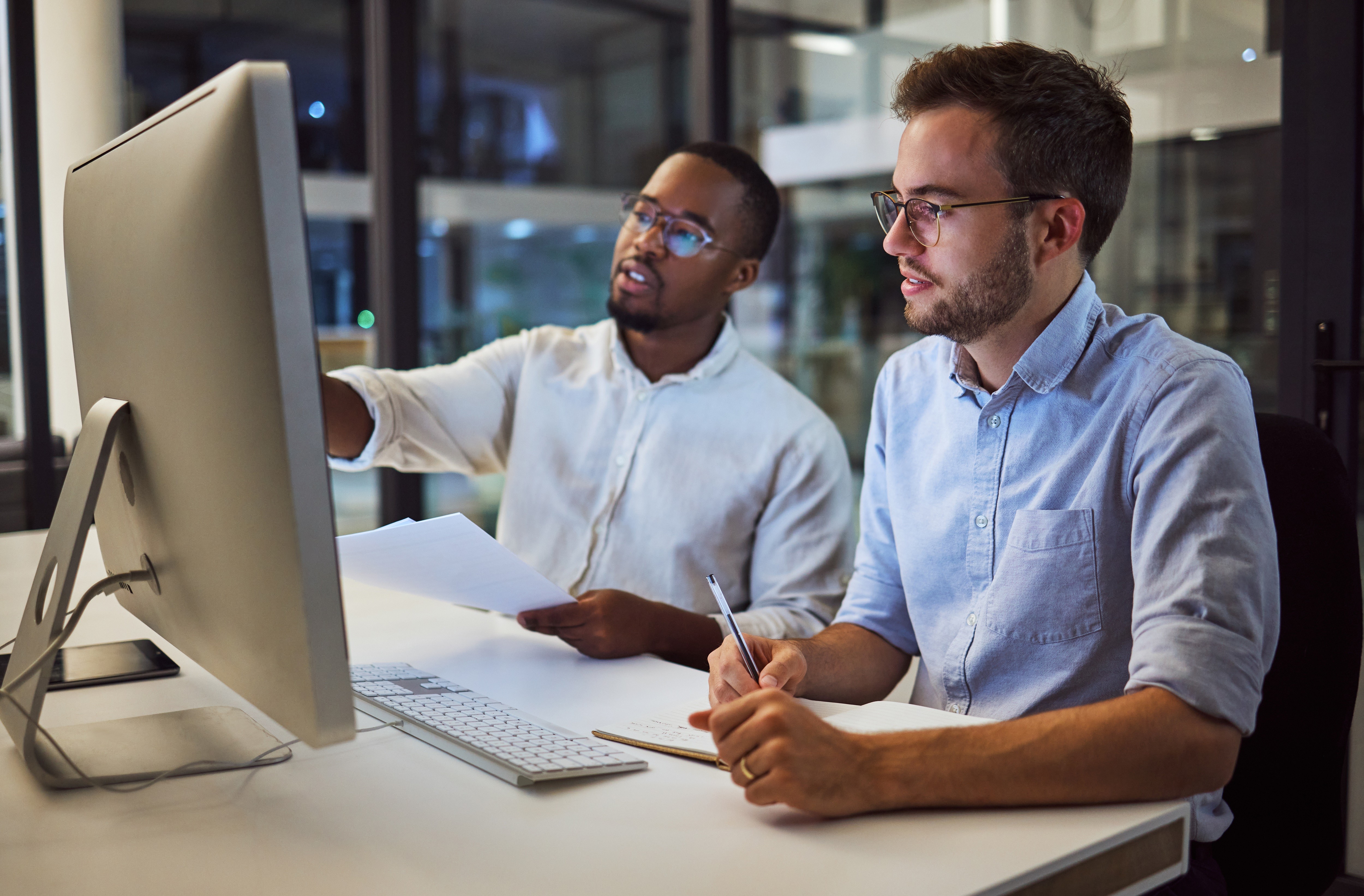 Auditor bespricht korrigierende Maßnahmen mit Prozessverantwortlichen in einem Büro, was die Prüfung der Wirksamkeit von Korrekturmaßnahmen, die Ursachenanalyse und die kontinuierliche Verbesserung in ISO-Managementsystemstandards darstellt.