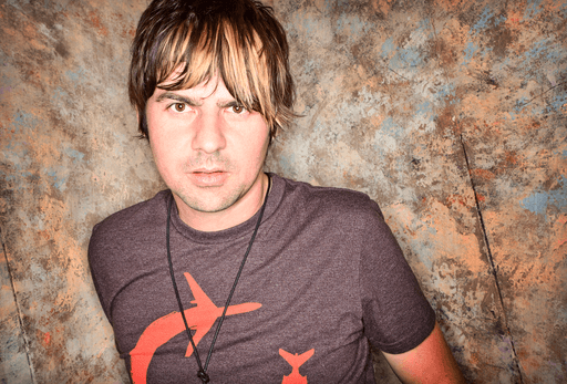 Editorial portrait of Australian singer Anthony Snape standing against a textured studio backdrop, looking directly at the camera.