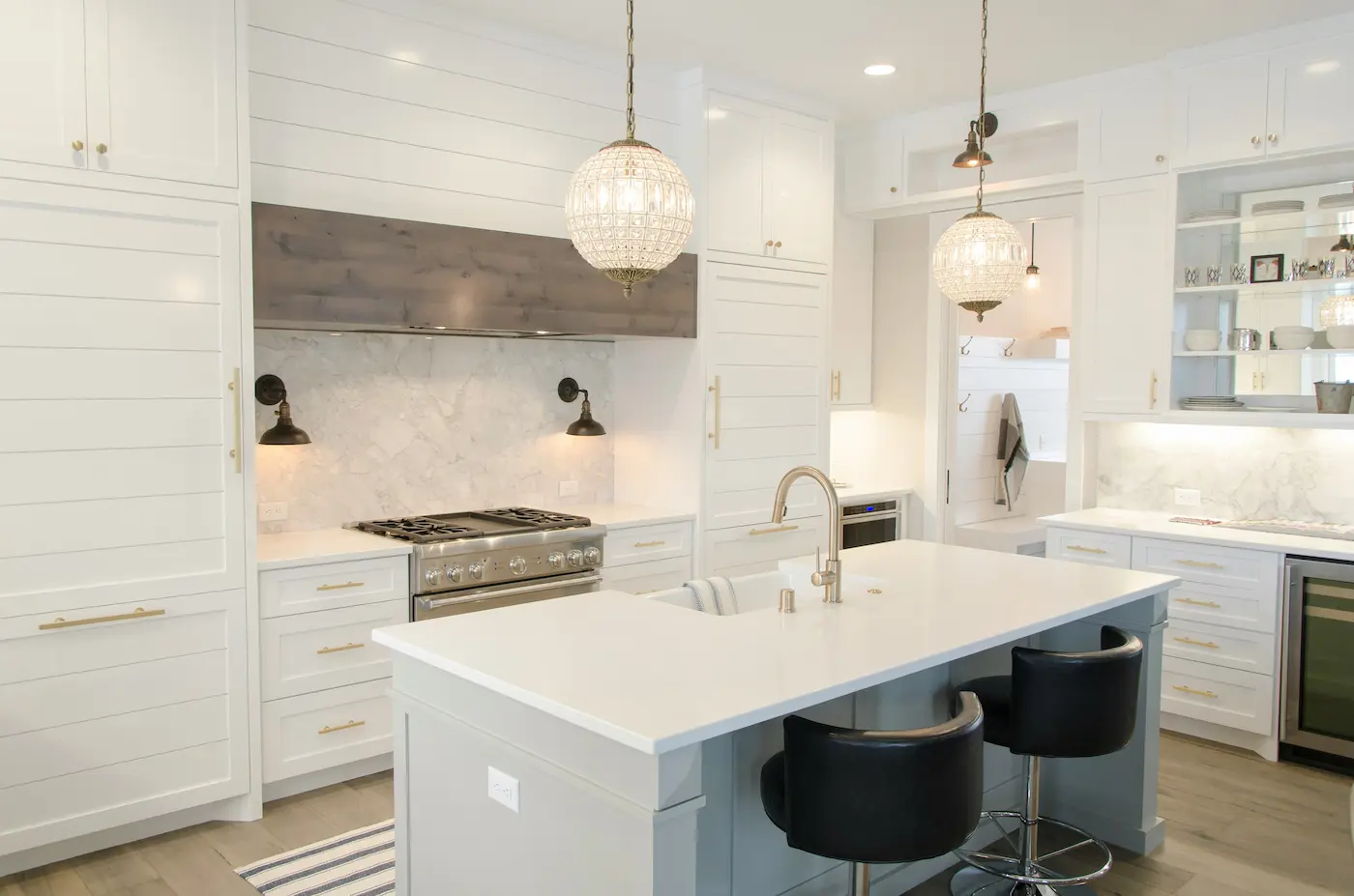 A brand-new luxury kitchen after a post-construction clean, featuring dust-free white shiplap walls, polished marble backsplashes, and sparkling crystal pendant lights.
