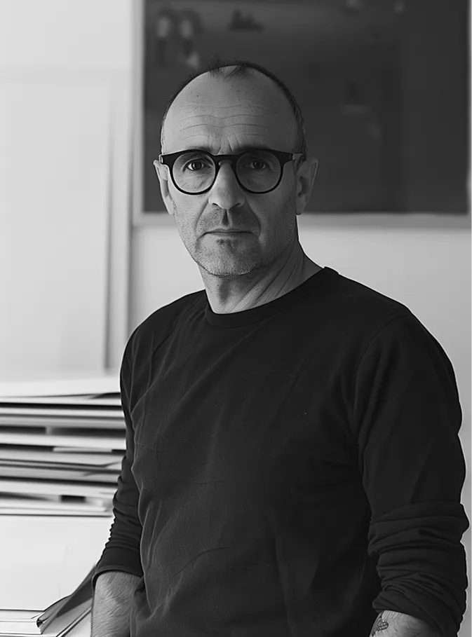 Middle-aged man with glasses in a dark shirt, standing in a room with artwork in the background, exuding a professional vibe.