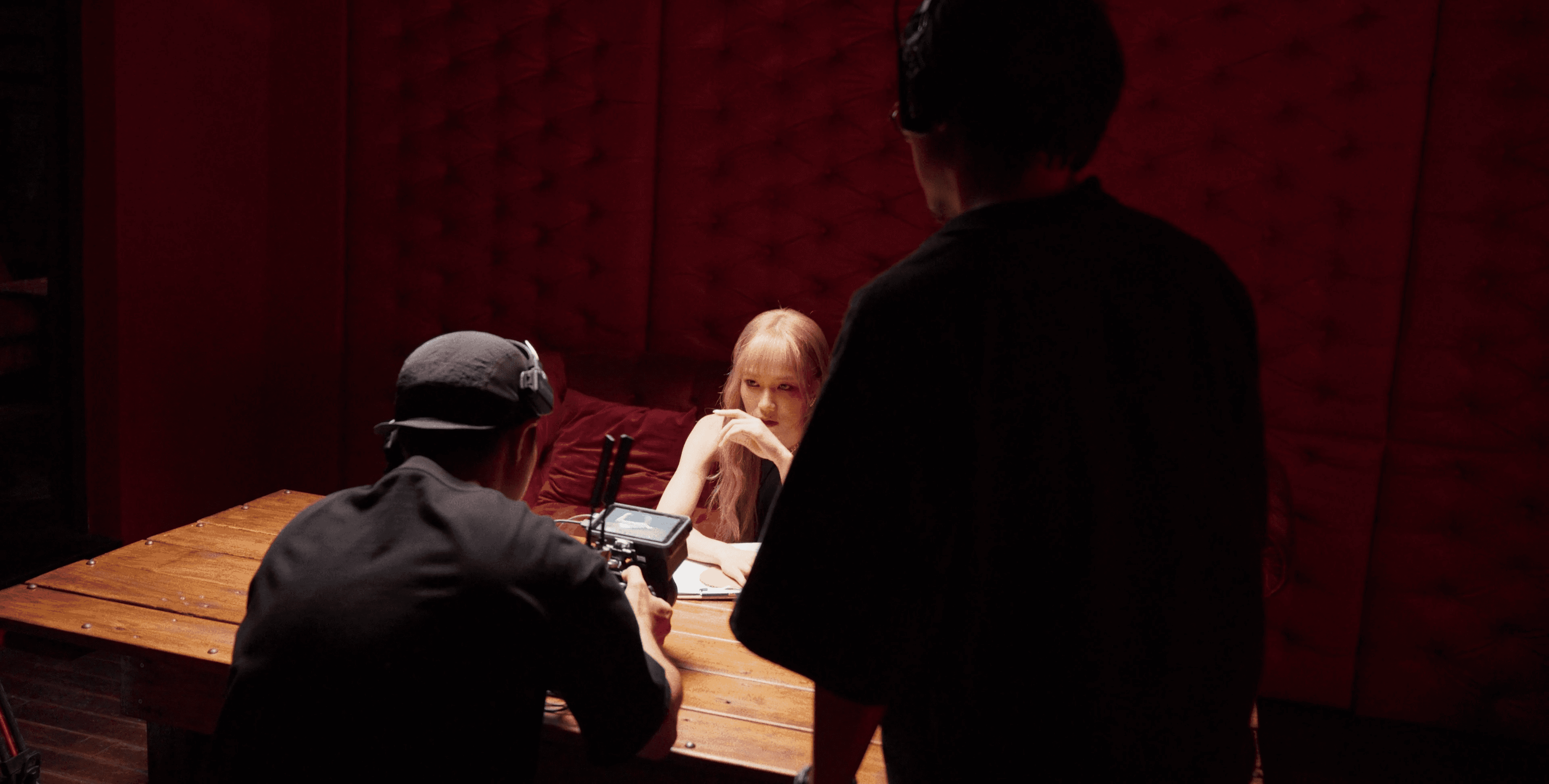 A film director sits in a chair facing a bustling, warmly lit night market scene. A camera setup is nearby, capturing the energetic atmosphere.